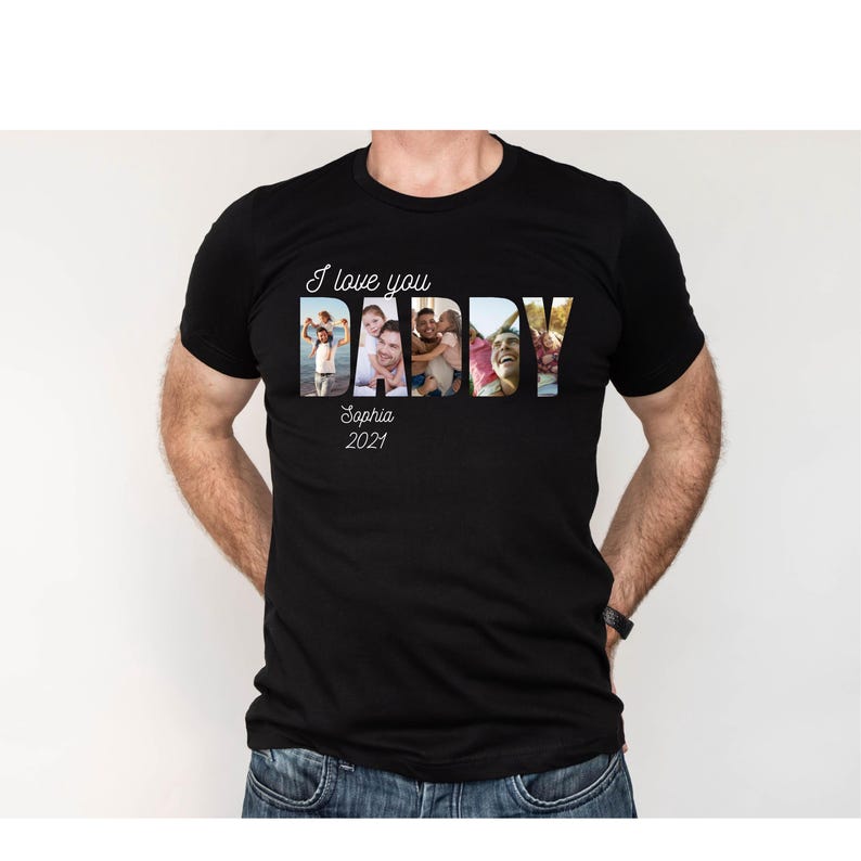 May include: Black t-shirt featuring the text "I love you DADDY" in white, with family photos filling the letters. The text "Sophia 2021" is below. The shirt is worn by a person, with blue jeans.