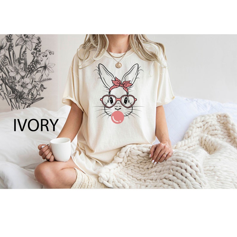 May include: A white t-shirt with a graphic of a bunny wearing pink glasses and a red bandana, blowing a pink bubble. The text "IVORY" is visible in the bottom left corner of the image.
