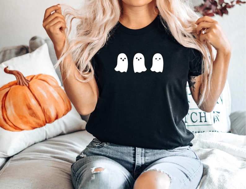 K&ouml;nnte beinhalten: Ein schwarzes T-Shirt mit einer wei&szlig;en Grafik von drei Geistern. Die Geister haben einfache, l&auml;chelnde Gesichter.