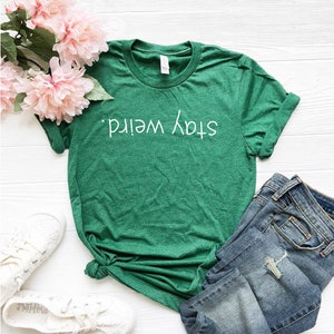 May include: Green t-shirt with the text "Stay Weird" in white lettering.