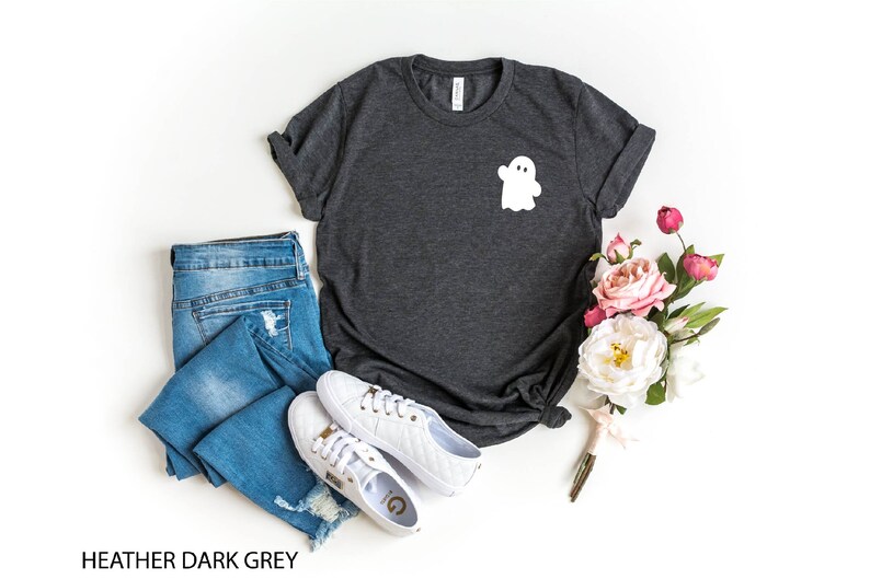 May include: Heather dark grey t-shirt with a white ghost graphic on the front. The shirt is paired with blue jeans and white sneakers.