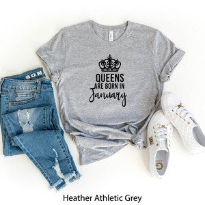 May include: Heather athletic grey t-shirt with a black crown and the text "Queens are born in January". The shirt is displayed with blue jeans and white sneakers.