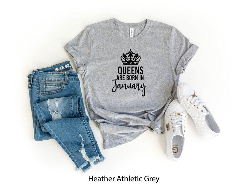 May include: Heather athletic grey t-shirt with a black crown and the text "Queens are born in January". The shirt is displayed with blue jeans and white sneakers.