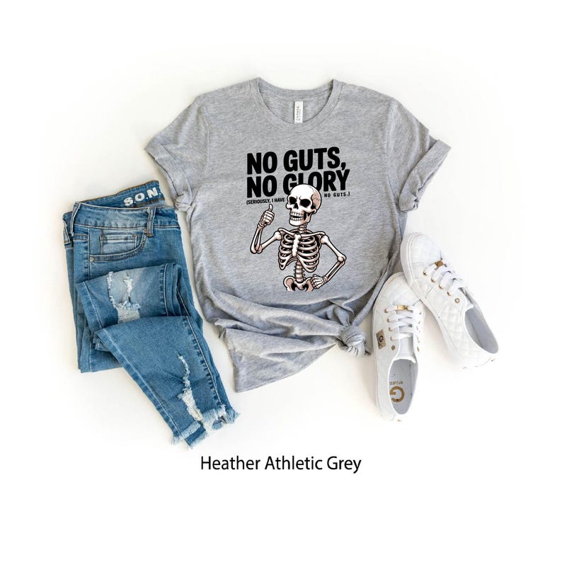 May include: A heather athletic grey t-shirt with the slogan "NO GUTS, NO GLORY" and a skeleton graphic. The image also shows a pair of blue jeans and white trainers.
