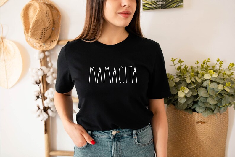 Może przedstawiać: Czarny t-shirt z nadrukiem "MAMACITA" w kolorze białym z przodu.