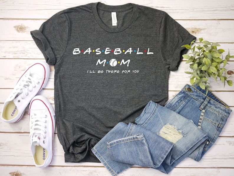 May include: A dark grey t-shirt with the text "BASEBALL MOM" in white with a baseball graphic. The text "I'LL BE THERE FOR YOU" is also in white below the main text.