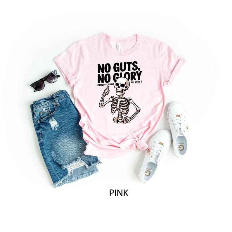 May include: A pale pink t-shirt featuring the slogan "NO GUTS, NO GLORY" and a skeleton illustration giving a thumbs up. The shirt is styled with blue denim shorts, white trainers, and black sunglasses. The word "PINK" is at the bottom.
