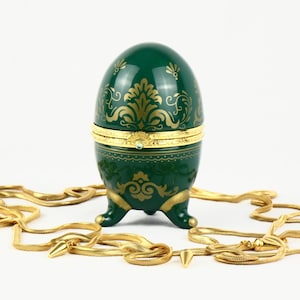 May include: A green porcelain egg-shaped trinket box with gold accents and a detailed floral design. The box is on three gold feet and has a hinged lid.