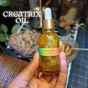 May include: A small glass bottle with a gold cap and a gold liquid inside. The bottle has a label that says "Creatrix Oil Soul Space".