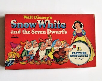 Puede incluir: Un conjunto de caja vintage de 11 figuras de plástico de Blancanieves y los Siete Enanitos de Walt Disney. La caja presenta un fondo rojo con ilustraciones de Blancanieves y los enanitos.