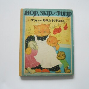 May include: A vintage children's book titled "Hop, Skip and Jump: Three Little Kittens". The cover features an illustration of three orange and white kittens. The book has a yellow background with a blue border.