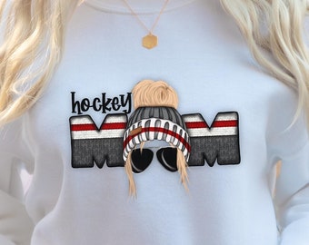 May include: White sweatshirt with a gray and black graphic of a woman wearing a winter hat and sunglasses with the text "hockey mom" above the graphic.