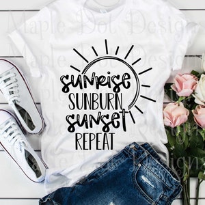 Könnte beinhalten: Weißes T-Shirt mit schwarzem Text, der "Sunrise Sunburn Sunset Repeat" lautet, und einer Sonnengrafik. Das Shirt liegt auf einer weißen Holzoberfläche mit einem Paar weißen Turnschuhen, einer blauen Jeans-Shorts und einem Strauß rosa und weißer Rosen.