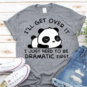 May include: Gray t-shirt with the text "I'll get over it, I just need to be dramatic first" and a cartoon panda bear graphic. White sneakers and denim shorts are also visible.