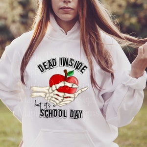 May include: White hoodie with a graphic of a skeleton hand holding a red apple with the text "Dead Inside but it's a School Day" printed on it.