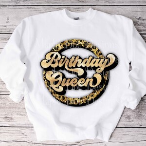 K&ouml;nnte beinhalten: Wei&szlig;er Pullover mit einem goldenen und schwarzen Kreisdesign, auf dem in goldener Schrift "Birthday Queen" steht.