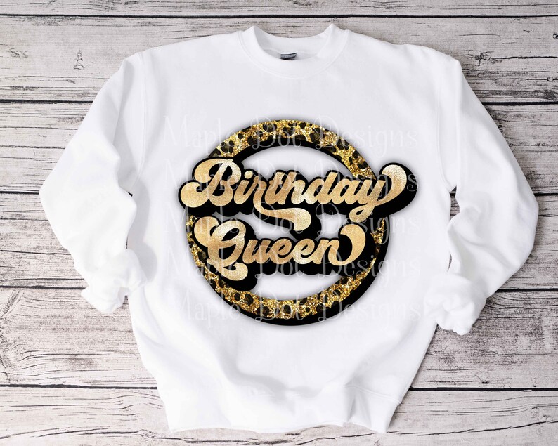 K&ouml;nnte beinhalten: Wei&szlig;er Pullover mit einem goldenen und schwarzen Kreisdesign, auf dem in goldener Schrift "Birthday Queen" steht.