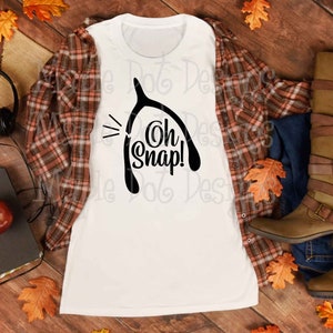 May include: White t-shirt with a black silhouette of a wishbone and the text "Oh Snap!" printed on it.