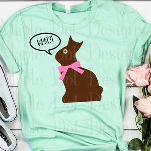 May include: A light blue t-shirt with a brown chocolate bunny wearing a pink bow and a speech bubble that says "WHAT?!".