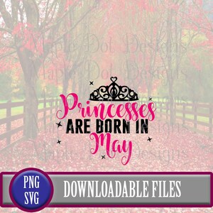 May include: Pink text on a black background with a black crown reads "Princesses are born in May". The background is a blurry image of a wooden fence and autumn foliage.