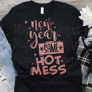 May include: Black t-shirt with the text "new year same hot mess" in a glittery rose gold font. The design includes stars and a rectangular box with the word "same". The shirt is folded with a pair of jeans and a scarf.