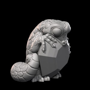 May include: A gray, 3D printed figurine of a frog holding a large, gray, geometric gem. The frog has a textured, scaly body and large, round eyes.