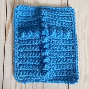 May include: A blue crocheted cross with a textured design. The cross is made with a single crochet stitch and has a raised center.