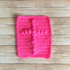 May include: A pink crocheted square with a raised cross design. The square is made with a single crochet stitch and has a textured look.