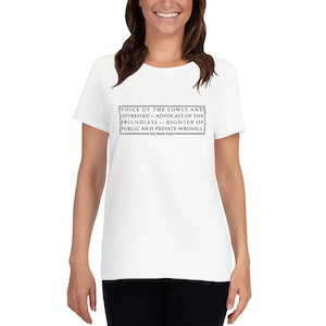Könnte beinhalten: Ein weißes T-Shirt mit einem schwarzen rechteckigen Textfeld mit dem Text "VOICE OF THE LOWLY AND OPPRESSED...RIGHTER OF PUBLIC AND PRIVATE WRONGS". Das T-Shirt hat einen Rundhalsausschnitt und kurze Ärmel.
