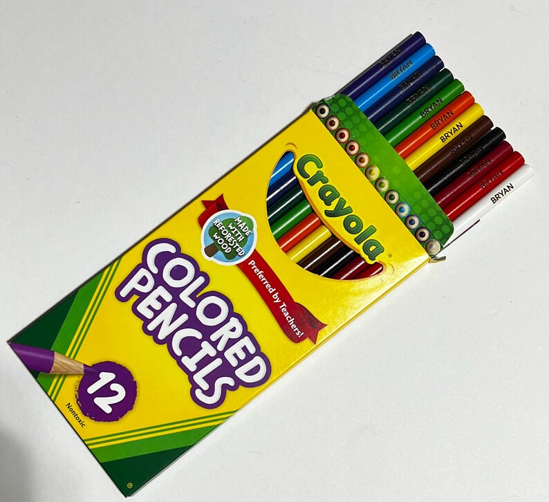 Puede incluir: Una caja amarilla Crayola con 12 l&aacute;pices de colores, con las palabras "COLORED PENCILS" en letras moradas grandes. La caja est&aacute; abierta, revelando los l&aacute;pices en varios colores. La caja tambi&eacute;n dice "Preferred by Teachers!"