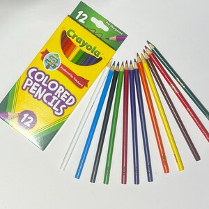 Puede incluir: Una caja amarilla y verde de 12 l&aacute;pices de colores Crayola preafilados, con las palabras "COLORED PENCILS" y "Crayola" impresas en la caja. Los l&aacute;pices est&aacute;n dispuestos en forma de abanico, mostrando una variedad de colores.