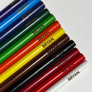 Puede incluir: Una colecci&oacute;n de diez l&aacute;pices de colores en varios tonos, incluyendo azul, verde, rojo y marr&oacute;n. Cada l&aacute;piz est&aacute; etiquetado con el nombre "BRYAN" en letras doradas. Los l&aacute;pices est&aacute;n dispuestos en diagonal, mostrando sus colores vibrantes.