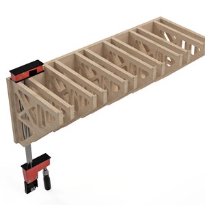 May include: A light-colored wooden shelf with a geometric design, held together by red and black clamps. The shelf has multiple compartments and is likely for storage or display. The clamps are positioned at the end of the shelf.