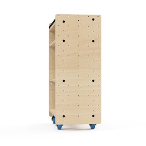 Puede incluir: Una estanter&iacute;a rodante de madera clara con cuatro estantes y una parte superior negra. Los estantes tienen agujeros para accesorios de tablero de clavijas. La unidad tiene cuatro ruedas azules.