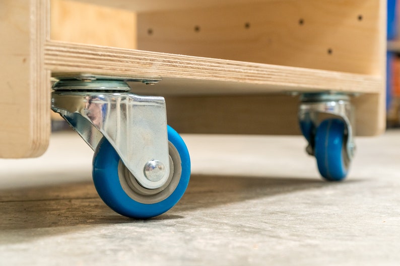 Puede incluir: Primer plano de un estante de madera con dos ruedas giratorias azules. Las ruedas son de metal y tienen una rueda de goma azul.