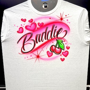 Cherry Airbrush design on a white shirt zoomed out. Baddie with black lettering and red with pink background.
