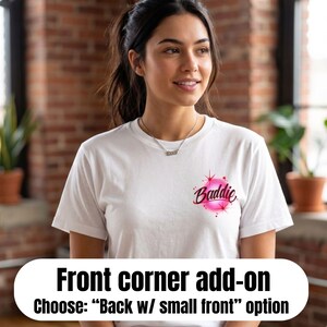 Pu&ograve; includere: Una t-shirt bianca a maniche corte con una piccola grafica sulla parte superiore sinistra del petto. La grafica consiste in un design circolare aerografato rosa brillante con la parola Baddie scritta in corsivo scuro, accentuata da stelle rosse.