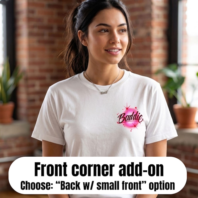 Pu&ograve; includere: Una t-shirt bianca a maniche corte con una piccola grafica sulla parte superiore sinistra del petto. La grafica consiste in un design circolare aerografato rosa brillante con la parola Baddie scritta in corsivo scuro, accentuata da stelle rosse.