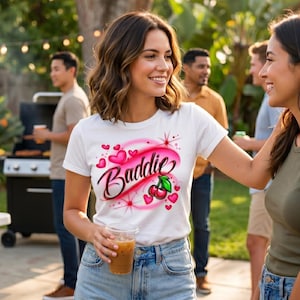 Young woman wearing a cherry Airbrush design on a white shirt at an afternoon gathering.
