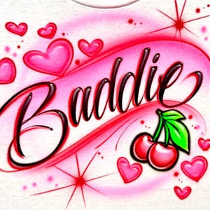 Cherry Airbrush design on a white shirt zoomed in. Baddie with black lettering and red with pink background.