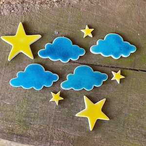 May include: A set of blue ceramic clouds and yellow ceramic stars. The clouds and stars are arranged on a wooden surface.