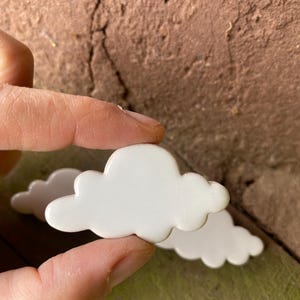 May include: Two white ceramic cloud-shaped ornaments. The clouds are smooth and have a slightly rounded shape.