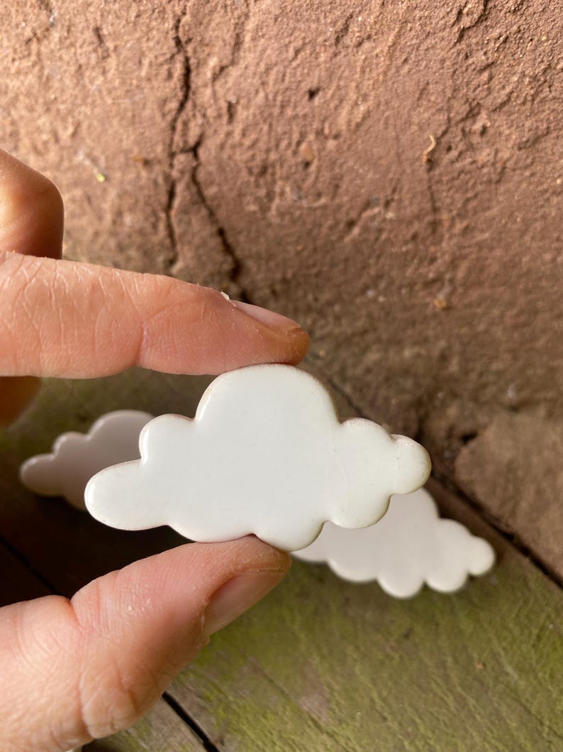 May include: Two white ceramic cloud-shaped ornaments. The clouds are smooth and have a slightly rounded shape.