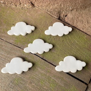May include: Five white ceramic cloud-shaped ornaments. The clouds are arranged in a staggered pattern on a wooden surface.