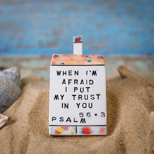 Puede incluir: Un adorno de cerámica blanca en forma de casa con un esmalte colorido. El adorno tiene el texto "WHEN I'M AFRAID I PUT MY TRUST IN YOU PSALM 56.3" escrito en él.