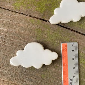 May include: White ceramic cloud shaped tiles, measuring approximately 6 cm in length. The tiles are arranged on a wooden surface with green moss.