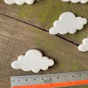 May include: Five white ceramic cloud-shaped tiles on a wooden surface. A ruler is in the foreground.