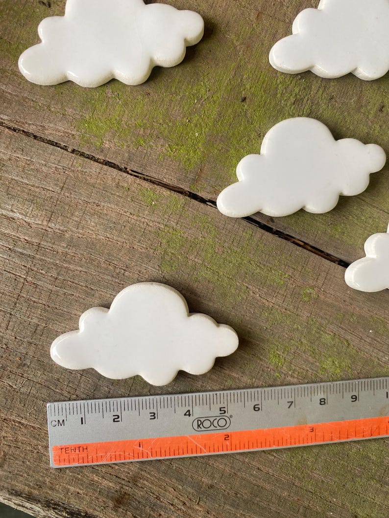 May include: Five white ceramic cloud-shaped tiles on a wooden surface. A ruler is in the foreground.