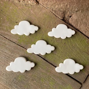 May include: Five white ceramic cloud-shaped ornaments on a wooden surface. The clouds are all the same size and shape, and they are arranged in a random pattern.