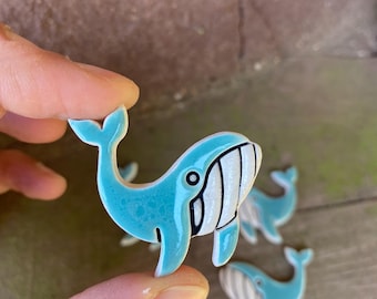 Könnte beinhalten: Ein Set aus vier Keramik-Walfiguren. Die Wale sind blau mit weißen Streifen und schwarzen Augen. Sie sind etwa 5 cm hoch.